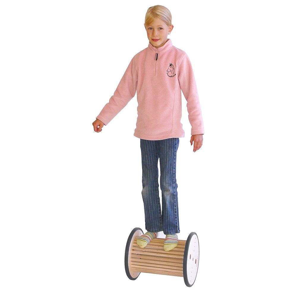 Kind steht auf einem Pedalo Pedasan 320. Das Gerät ist zylindrisch, aus Holz mit schwarzen Rändern. Das Kind trägt Jeans und ein rosa Oberteil.