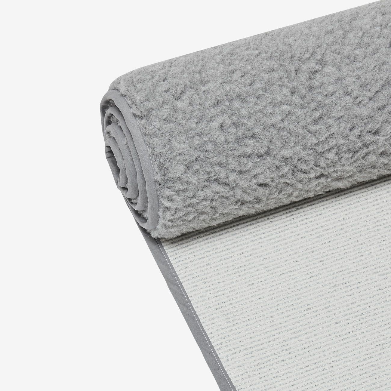 Gerollte Yogamatte aus Wolle. Graue Oberseite mit flauschiger Textur, grauer Rand. Unterseite sichtbar.