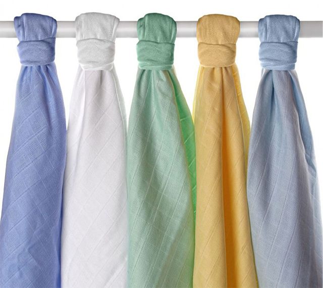 Fünf farbige Mullwindeln, an Stange aufgehängt. Farben: Blau, Weiß, Grün, Gelb, Blau. Stoffstruktur erkennbar.