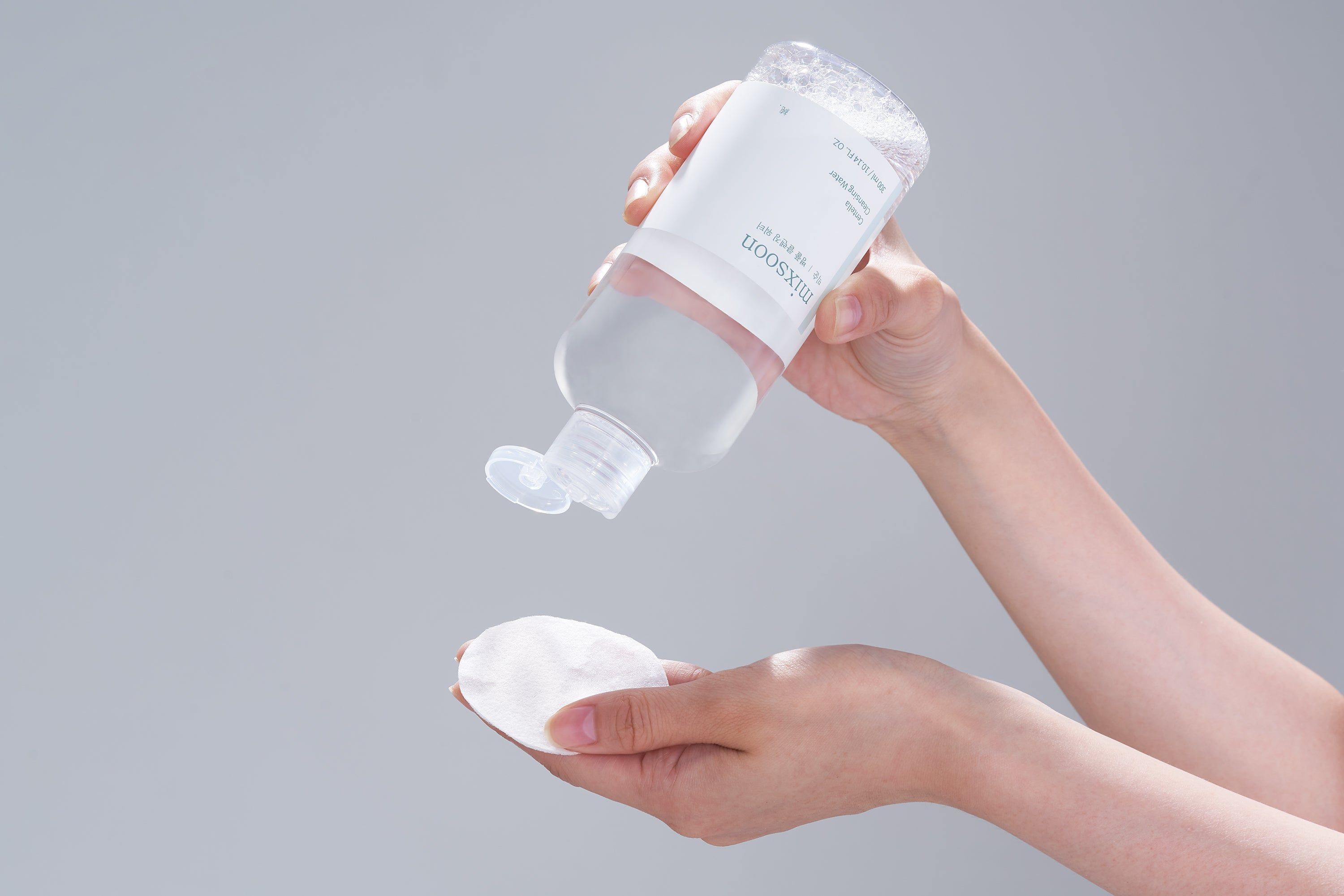 Hände halten Flasche und Wattepad. Flasche mit weißem Etikett. Aufschrift: mixsoon. Produkt auf hellem Hintergrund.