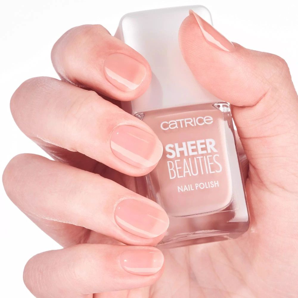 Hand mit lackierten Nägeln und Nagellackflasche. Aufschrift: CATRICE SHEER BEAUTIES NAIL POLISH.