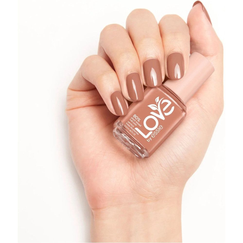 Hand hält Nagellackflasche. Nägel mit Nagellack lackiert. Aufschrift: Love by Essie. Rosa Deckel, quadratische Form.