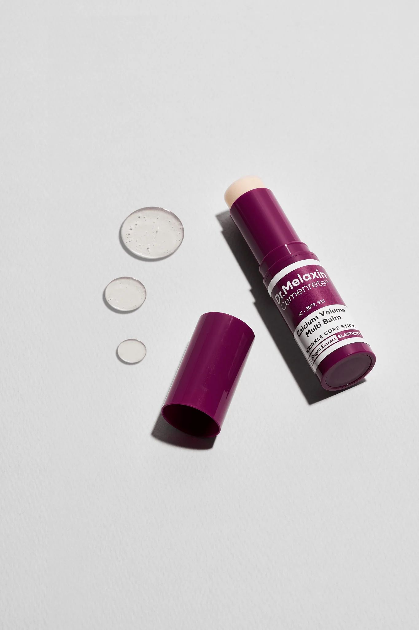 Dunkellila Balm mit geöffneter Kappe und Tropfen. Aufschrift: Dr.Melaxin Cemenrete Calcium Volume Multi Balm. Weißer Text.