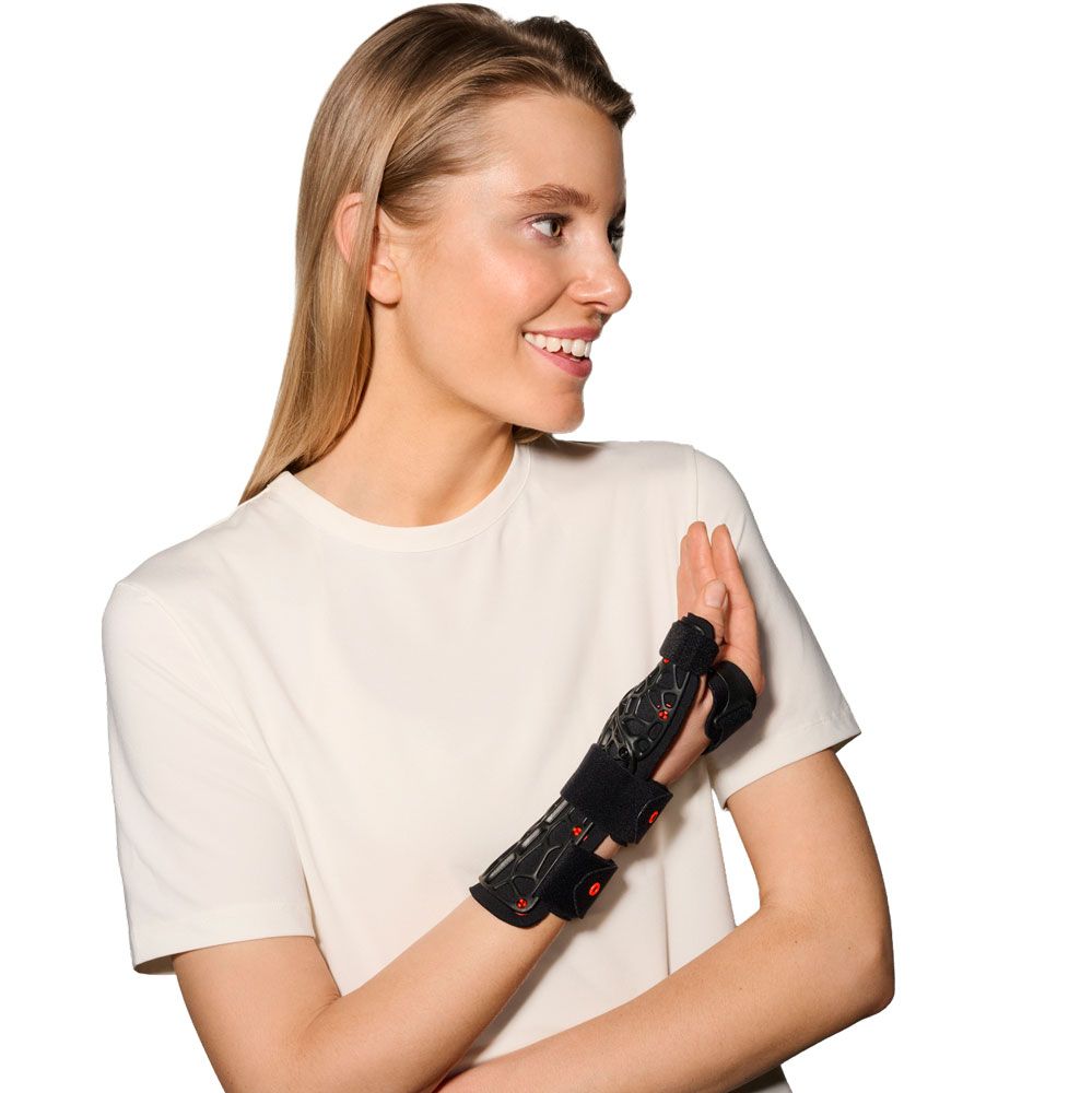 Frau trägt eine schwarze Handgelenkorthese mit Daumenfixierung, die mit Klettverschlüssen und einem Gittermuster versehen ist.