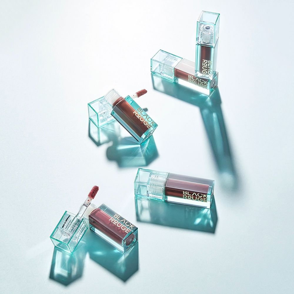 Mehrere Lipgloss-Behälter, teilweise geöffnet, auf einer hellblauen Oberfläche. Der Name BLACK ROUGE ist sichtbar.