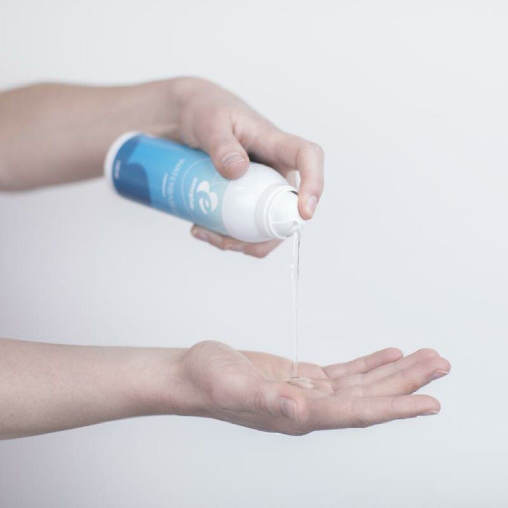 Person hält eine Flasche und gibt eine klare Flüssigkeit in die Handfläche. Die Flasche ist blau-weiß und trägt die Aufschrift "WATERBASED".