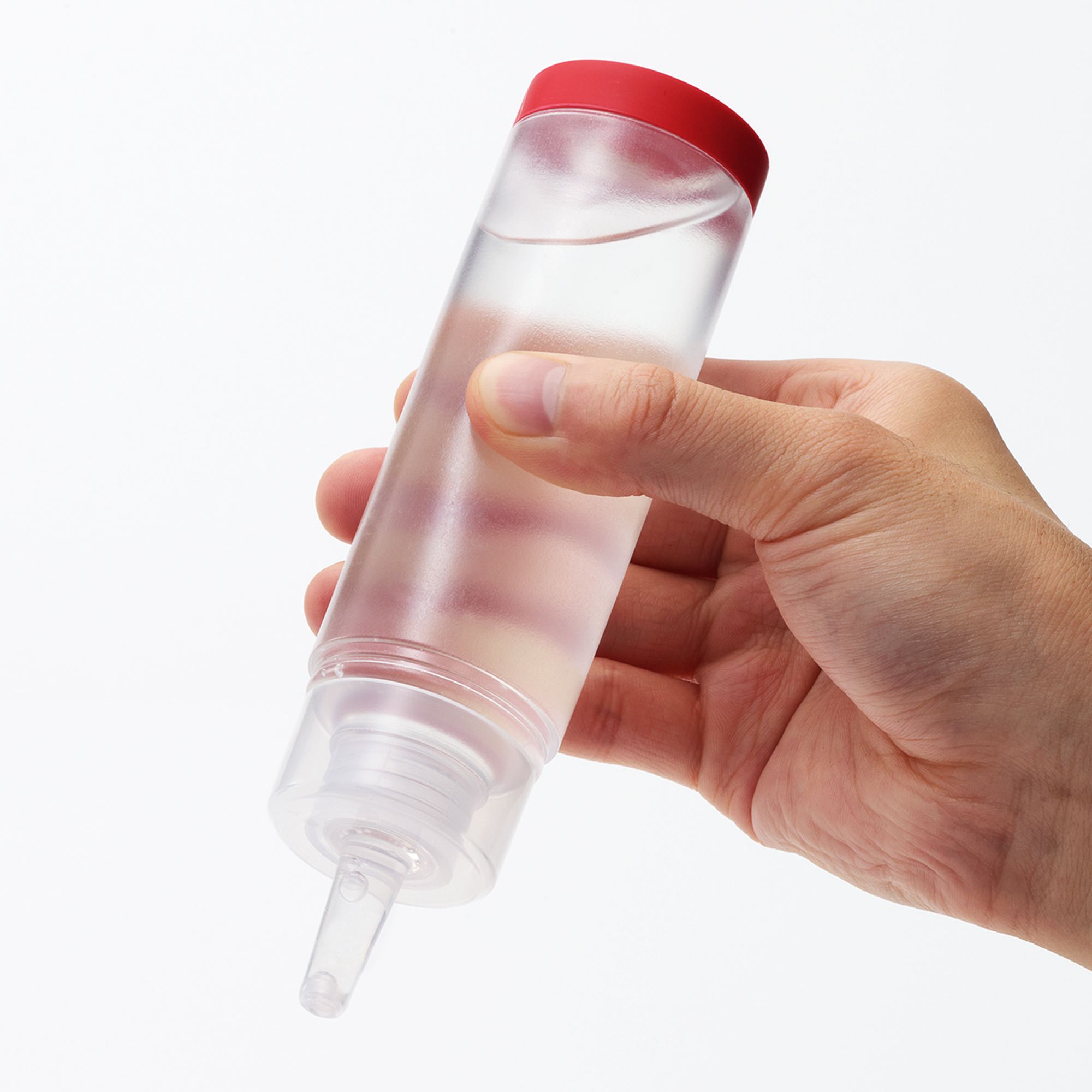 Durchsichtige Flasche mit rotem Deckel, gehalten von einer Hand. Der Inhalt ist klar.