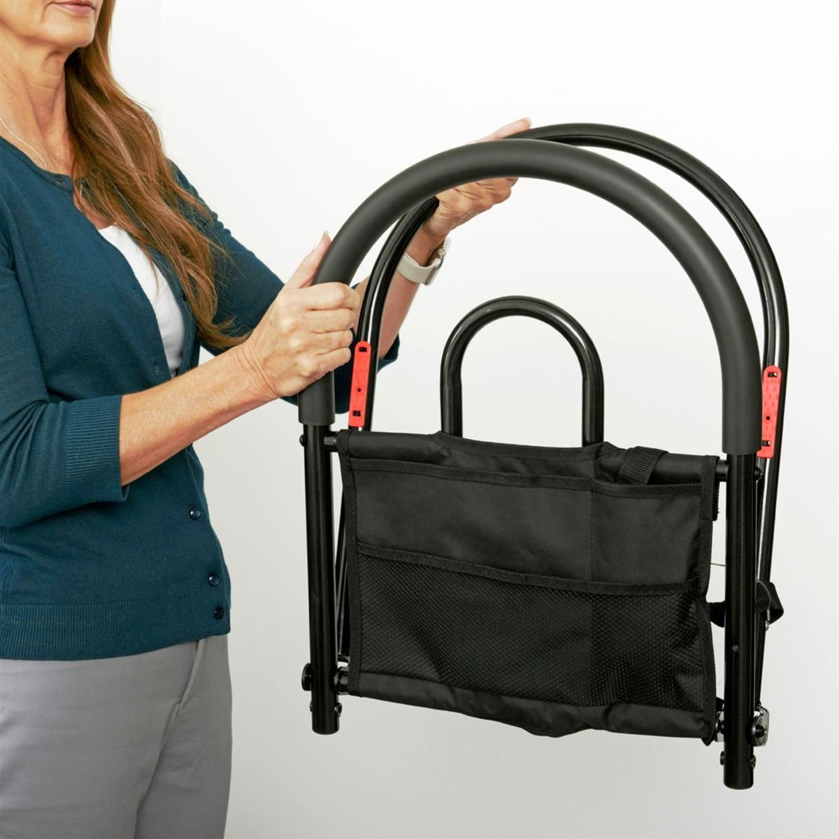 Person hält zusammengeklapptes schwarzes Bettgitter. Mit Griff und Tasche. Roter Knopf.