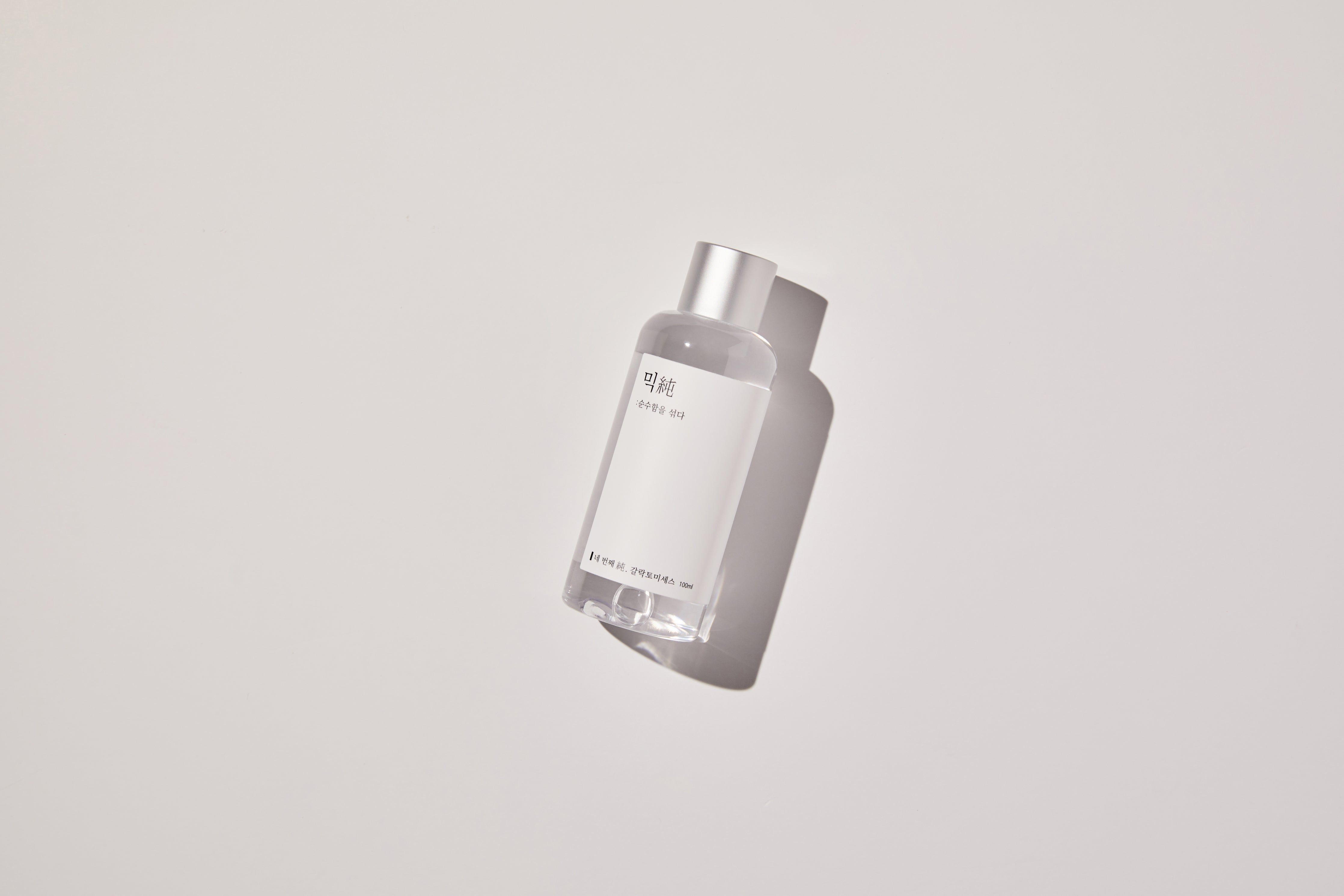 Klare Flasche mit silbernem Deckel und weißem Etikett. Auf weißem Hintergrund. Schattenwurf.