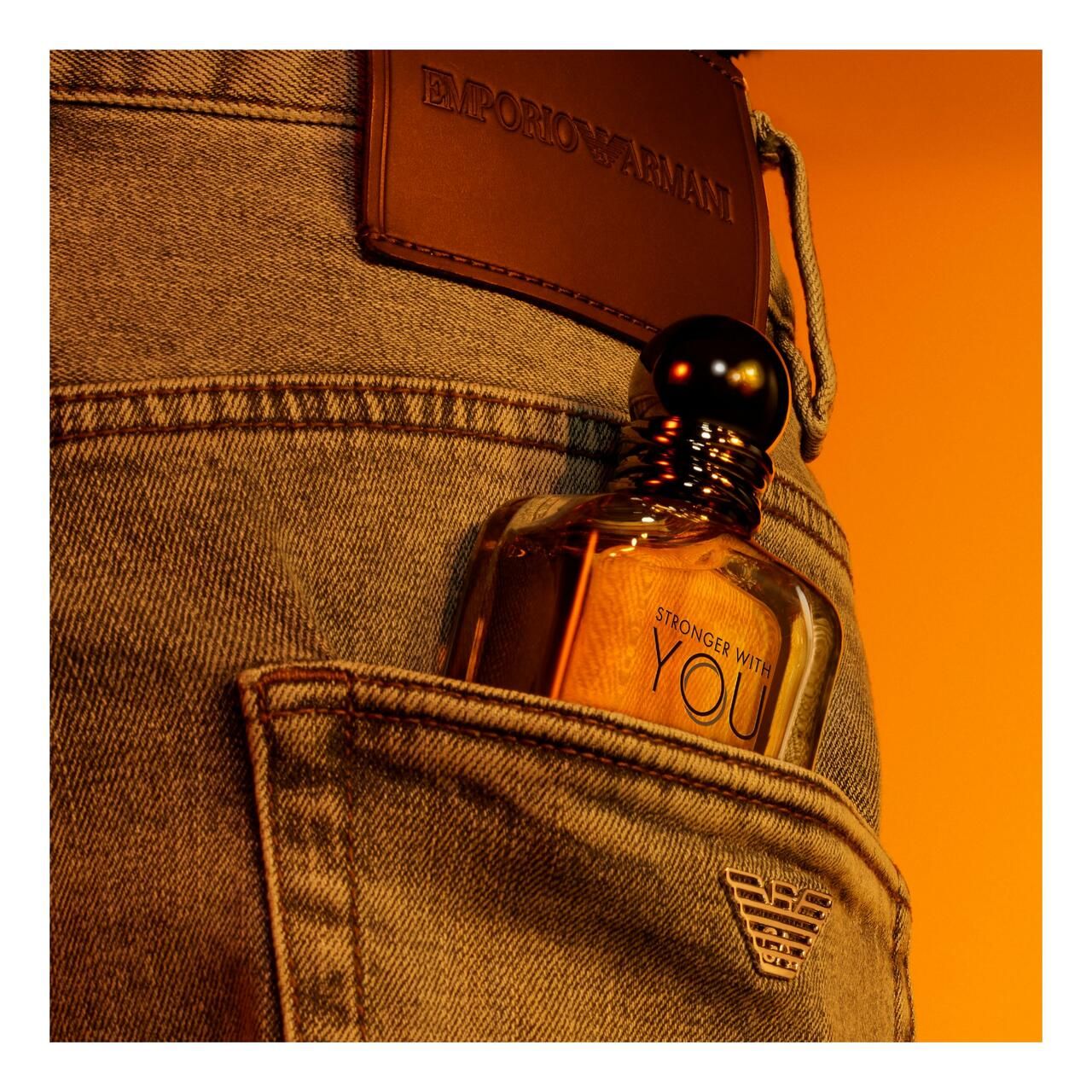 Glasflakon in Jeans-Hosentasche. Aufschrift: STRONGER WITH YOU und EMPORIO ARMANI. Leder-Label mit Logo.