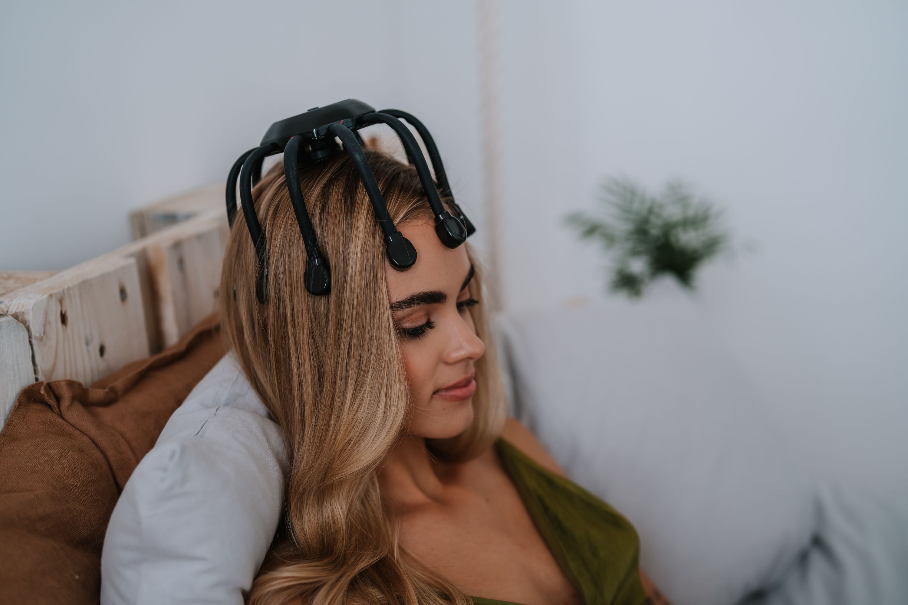 Frau mit blonden Haaren und einem schwarzen Kopfmassagegerät auf dem Kopf. Nahaufnahme.