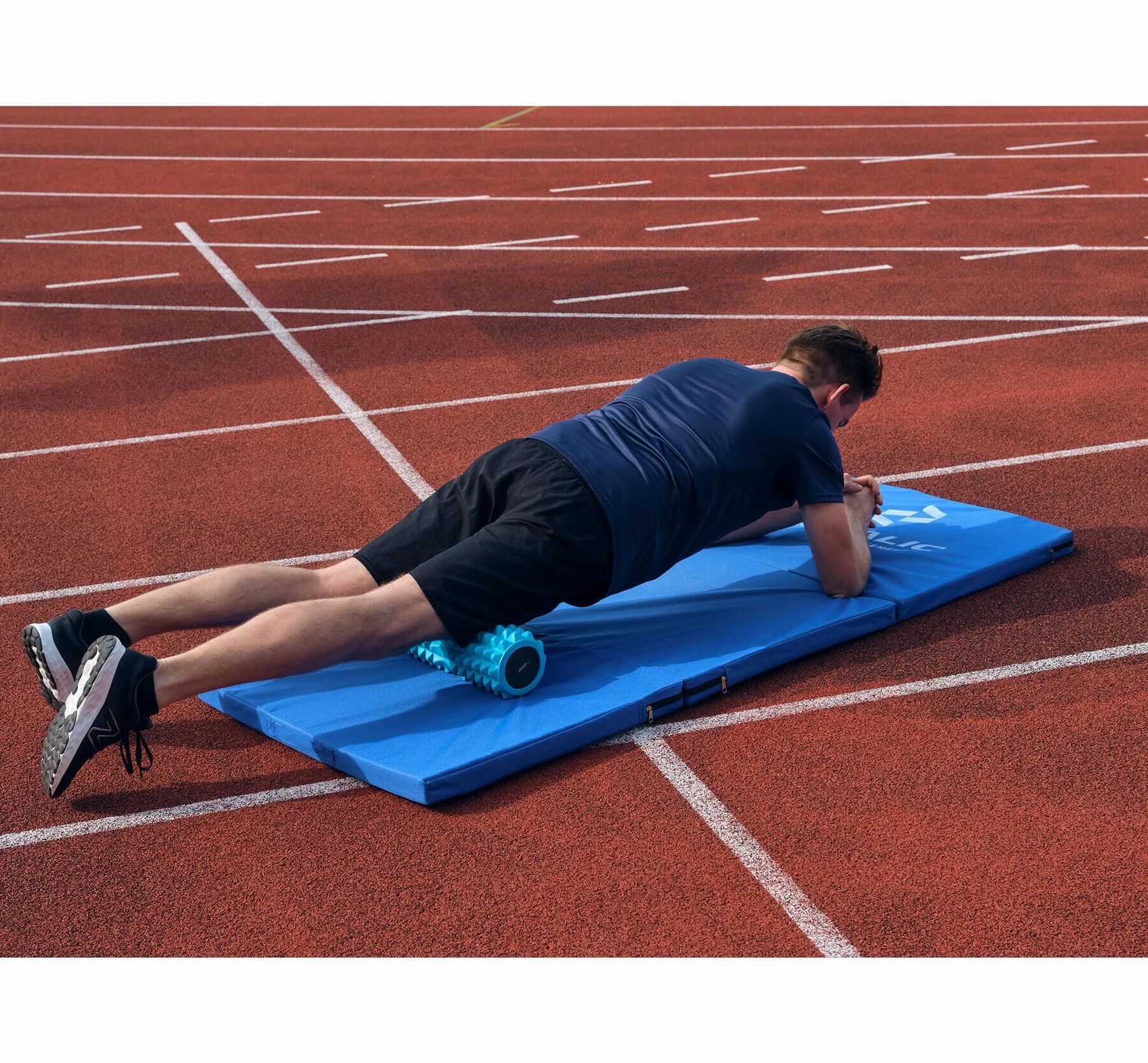 Person auf blauem Gymnastikmatte mit Faszienrolle. Auf roter Laufbahn. Matte mit Logo.