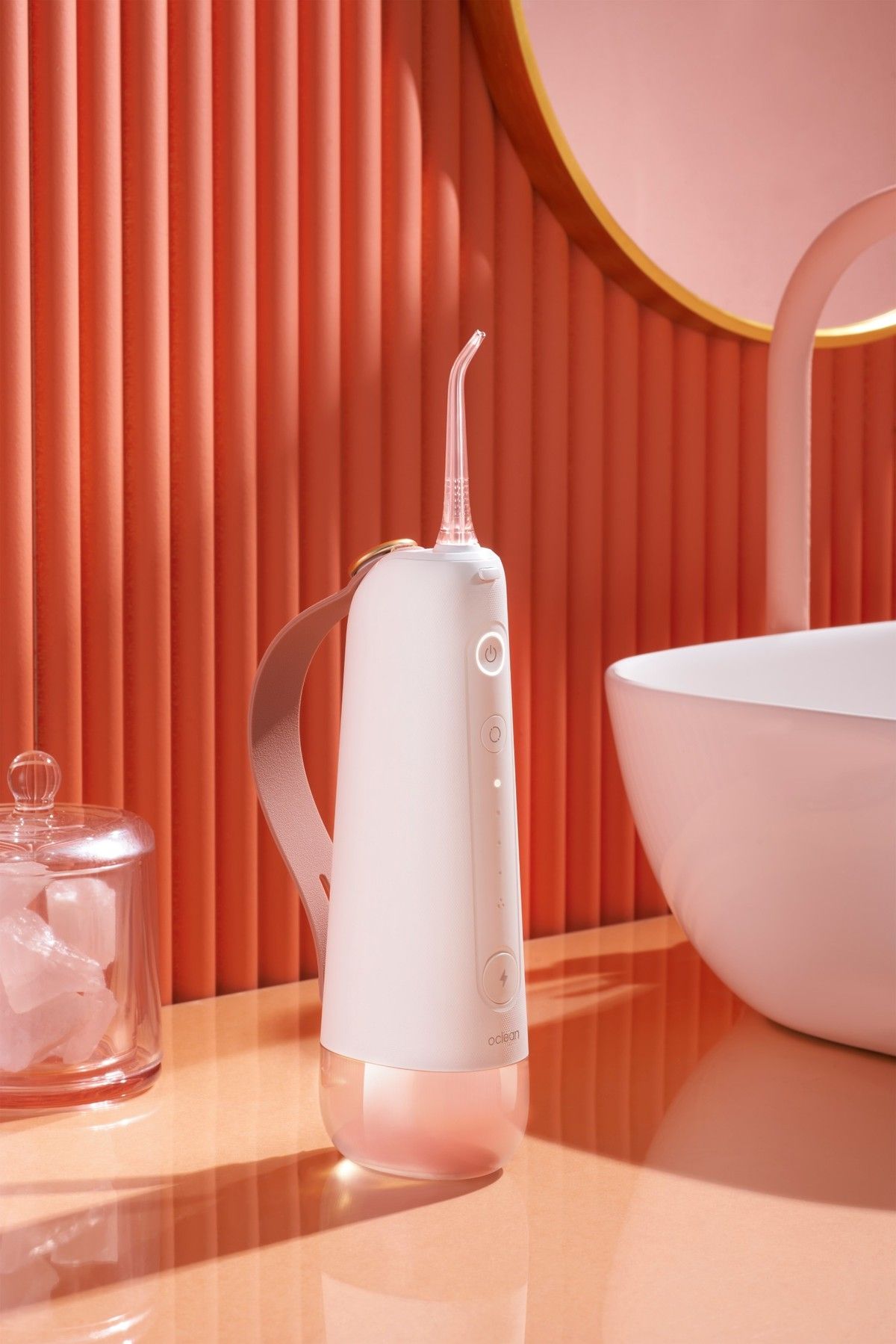 Weiß-rosafarbene Munddusche auf einer Oberfläche. Gerät mit Düse und Bedienknöpfen. Hintergrund: Waschbecken und Accessoires.