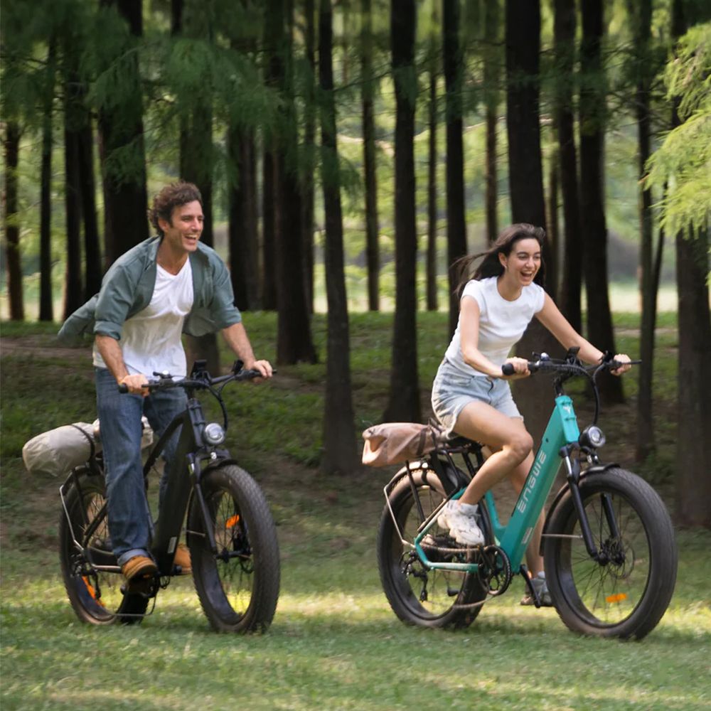 Zwei Personen fahren E-Mountainbikes auf einem Rasen. Beide Räder haben breite Reifen.