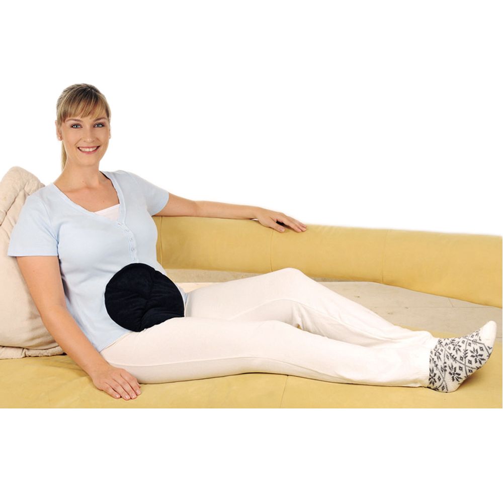 Eine Frau sitzt auf einem Sofa und hält ein schwarzes, rundes Kissen auf dem Bauch. Sie trägt helle Kleidung.