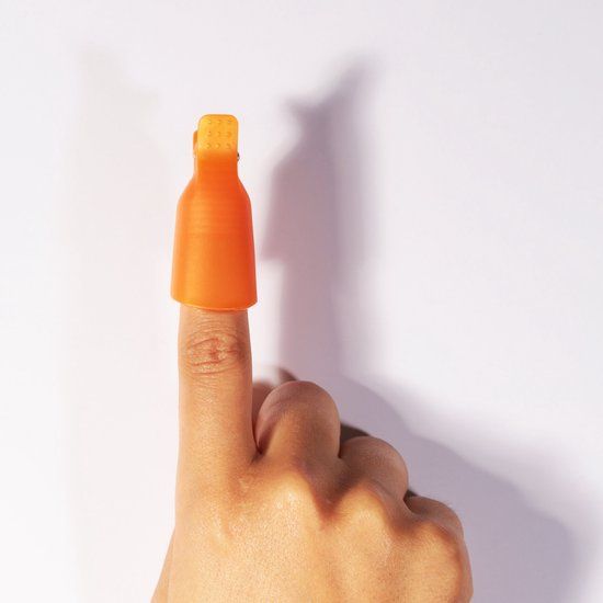 Ein oranger Clip auf einem Finger. Der Clip bedeckt den Nagel. Weißer Hintergrund.