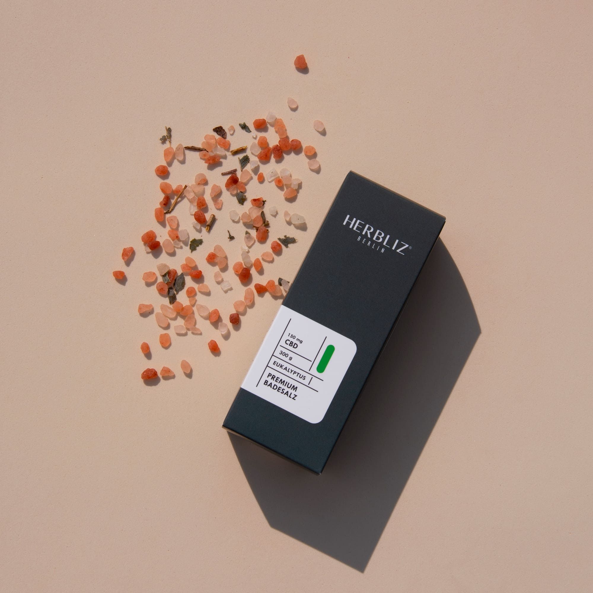 Dunkelgraue Verpackung mit Aufschrift: HERBLIZ, Eukalyptus, CBD, Badesalz. Umgeben von Badesalzkristallen.