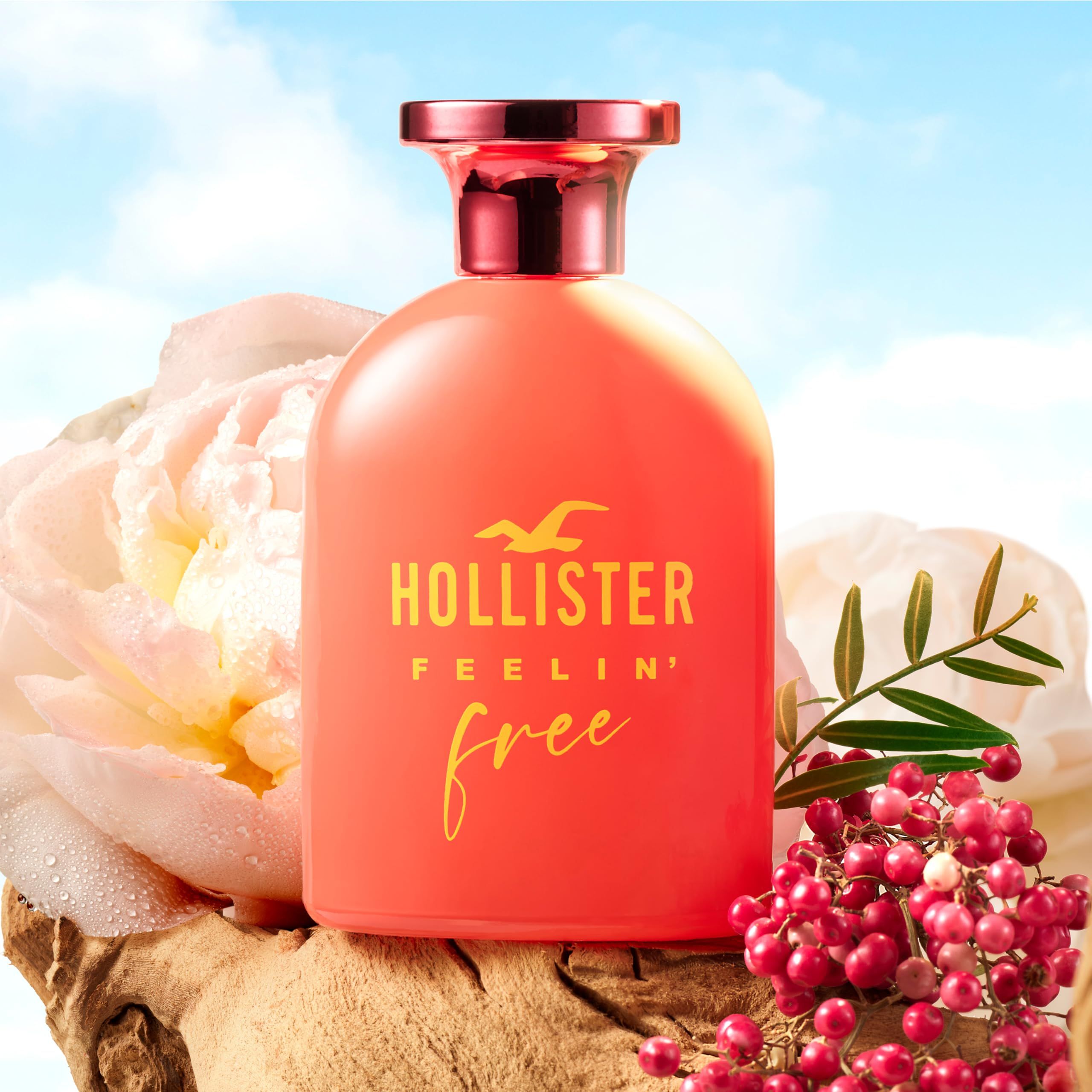 Roter Flakon mit gelbem Schriftzug. Aufschrift: Hollister Feelin' Free. Rosa Verschluss. Hintergrund: Blumen.