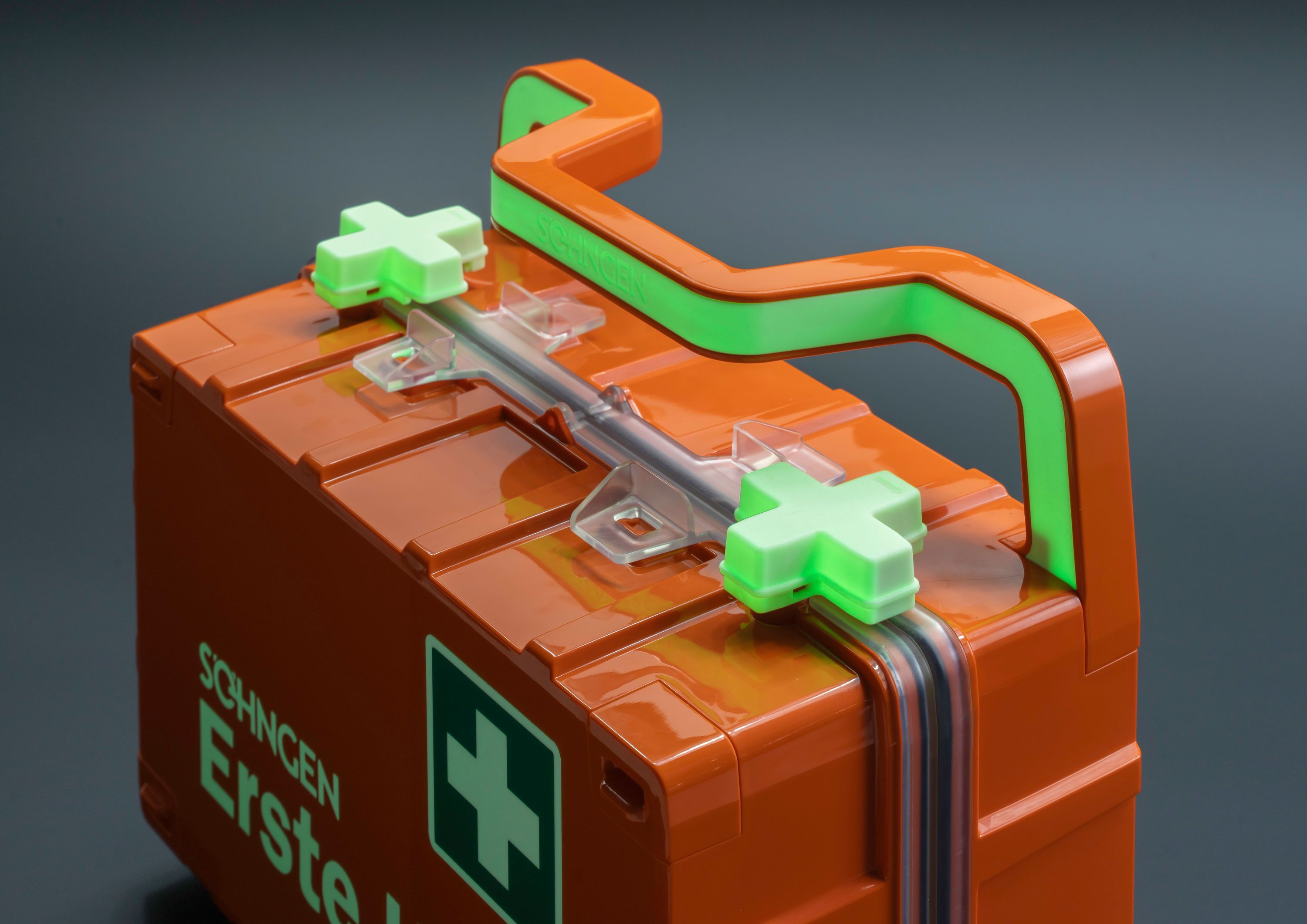 Orange Erste-Hilfe-Kasten mit grünem Griff und Kreuzsymbolen.