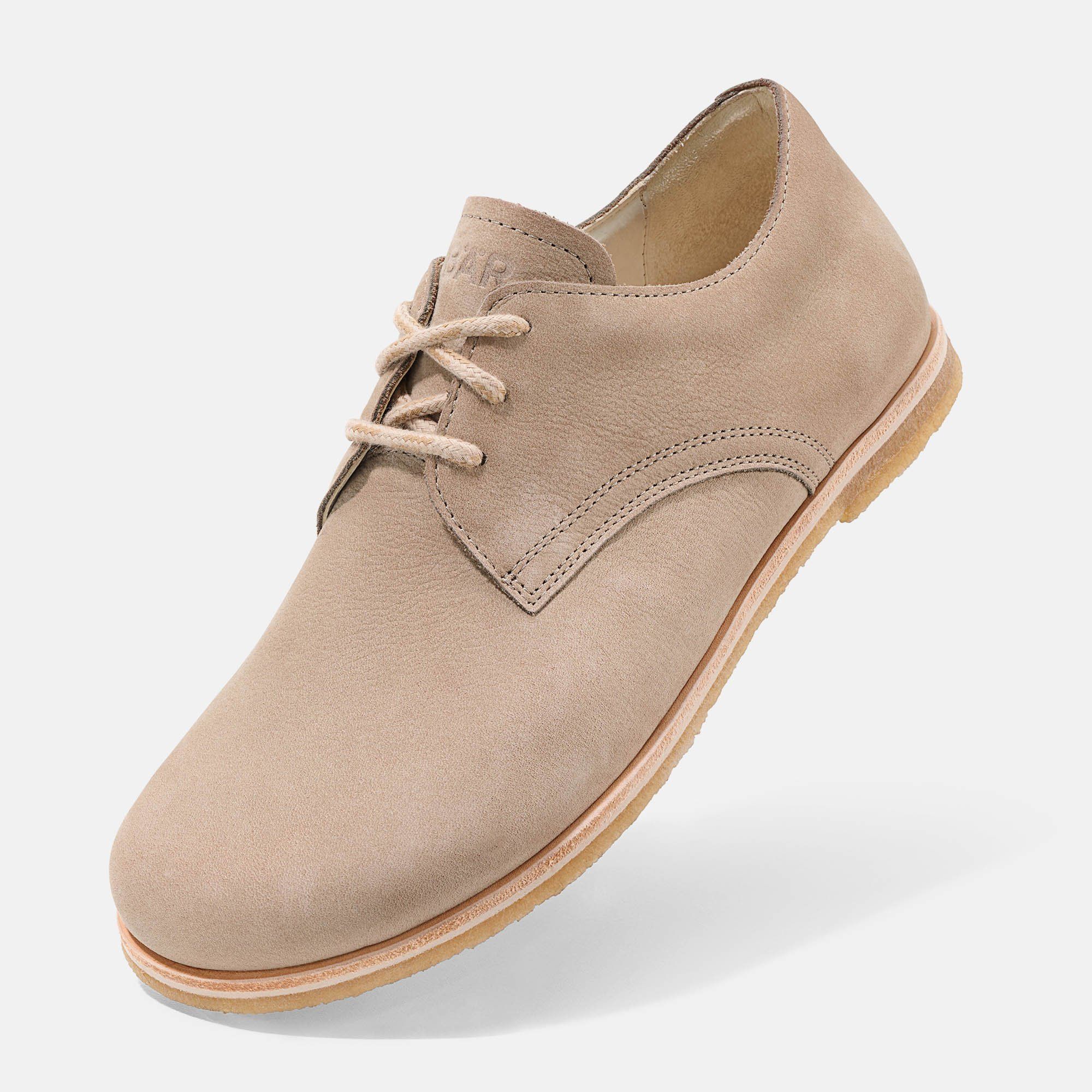 Beigefarbener Schnürschuh. Flache Sohle, helle Schnürsenkel. Schräge Ansicht.