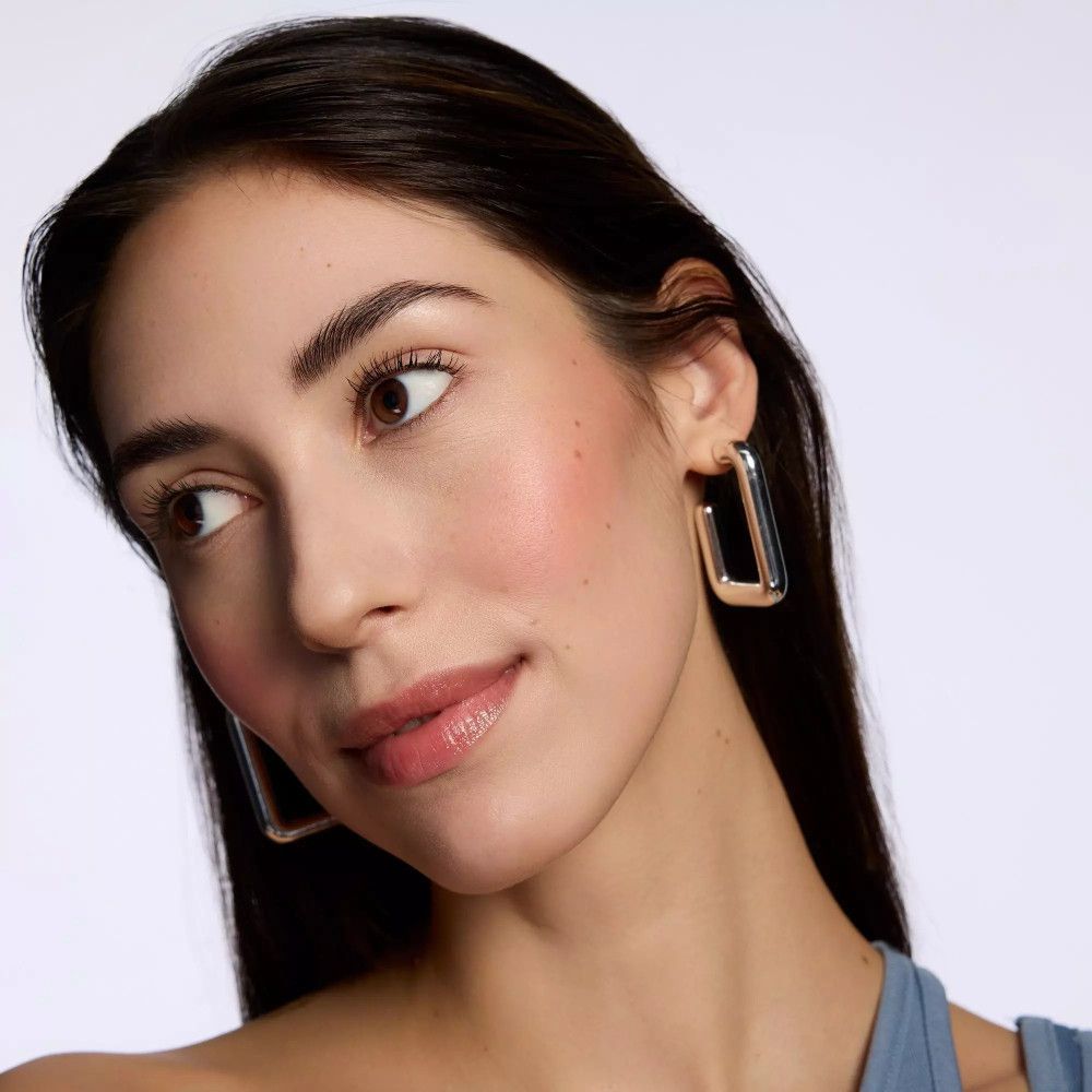 Porträt einer Frau mit Rouge auf den Wangen. Trägt Ohrringe. Blick zur Seite.