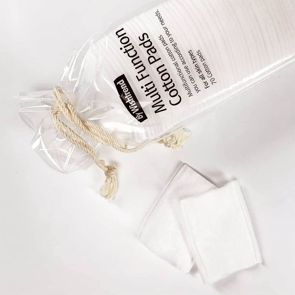 Aus der Verpackung entnommene, quadratische Baumwoll-Pads. Aufschrift: By Wishtrend Multi Function Cotton Pads. Transparente Verpackung.