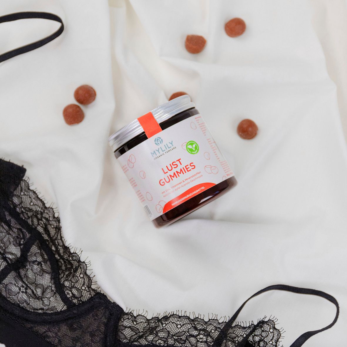 Glas MYLILY Lust Gummies auf weißem Stoff, daneben schwarzer BH und Gummibärchen.