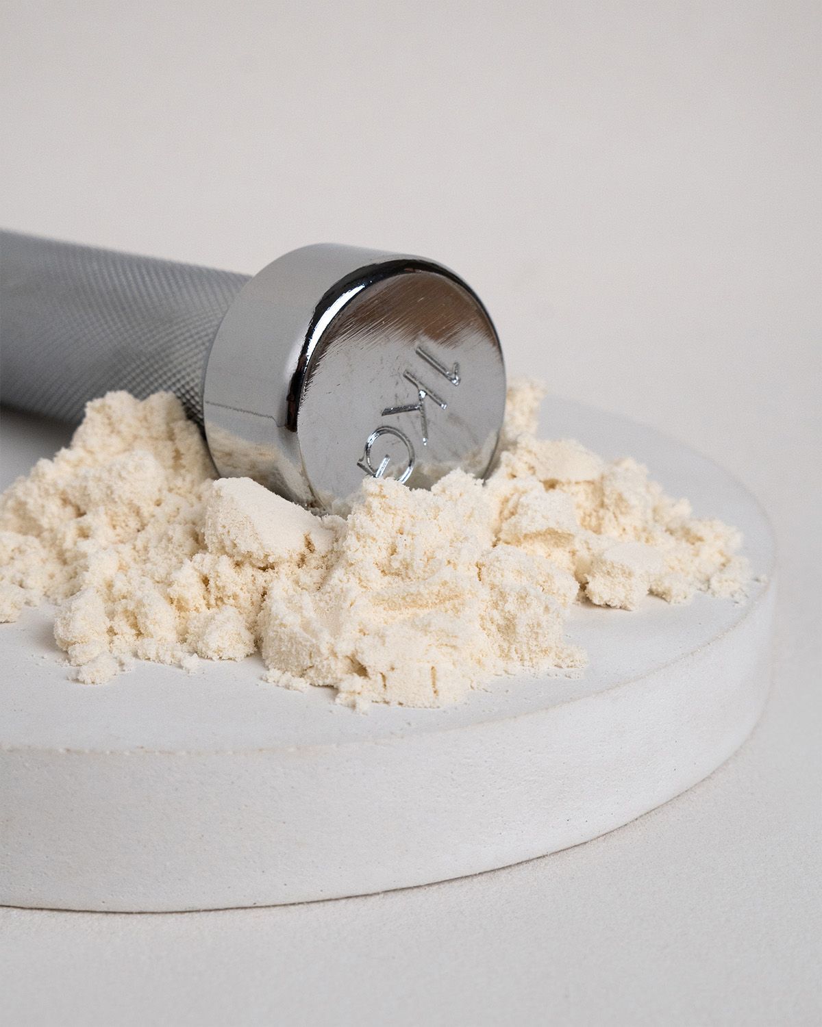 Hantel und Pulver auf weißem Podest. Hantel mit 1KG-Markierung. Helle, beige Pulvermasse.