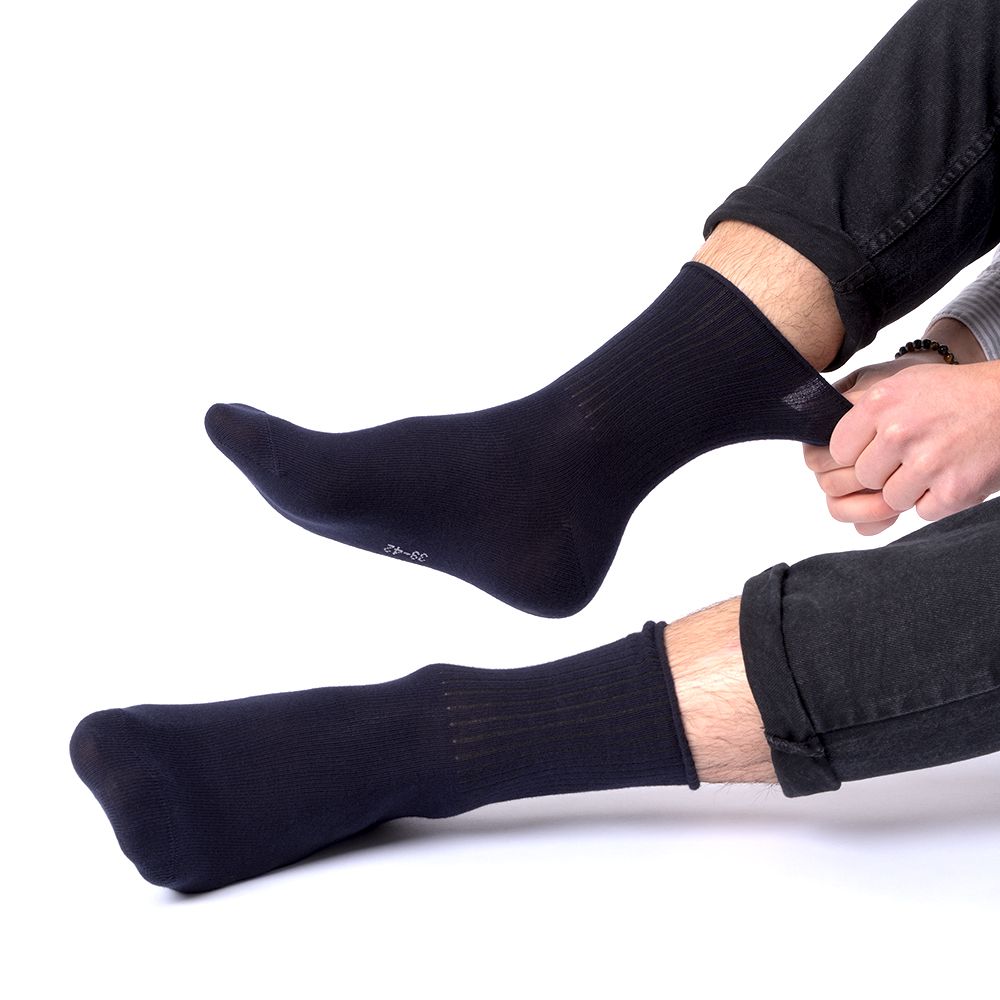 Person zieht schwarze Socke an. Rippstrickbündchen. Angenehmes Material. Füße auf hellem Hintergrund.