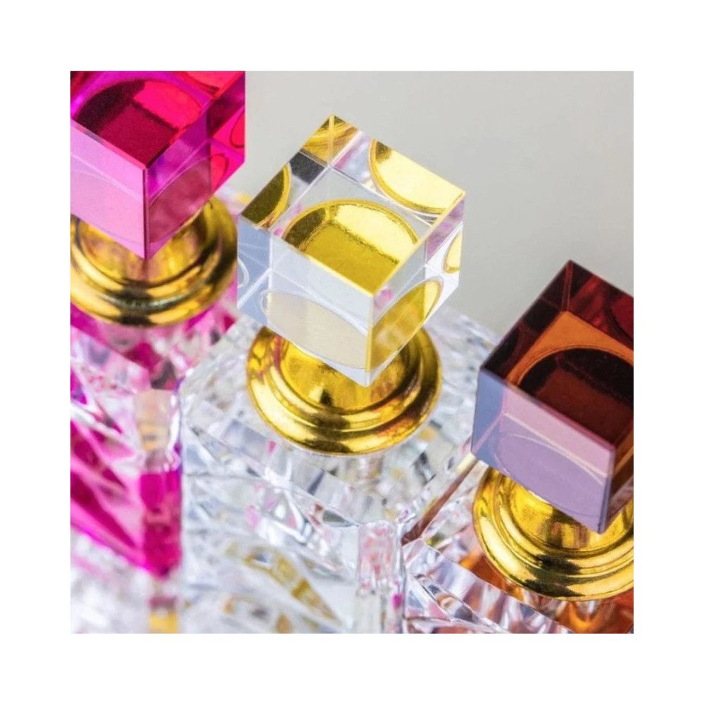 Nahaufnahme von drei Parfümflakons. Klare, facettierte Glasbehälter mit farbigen Deckeln und goldenen Basen.
