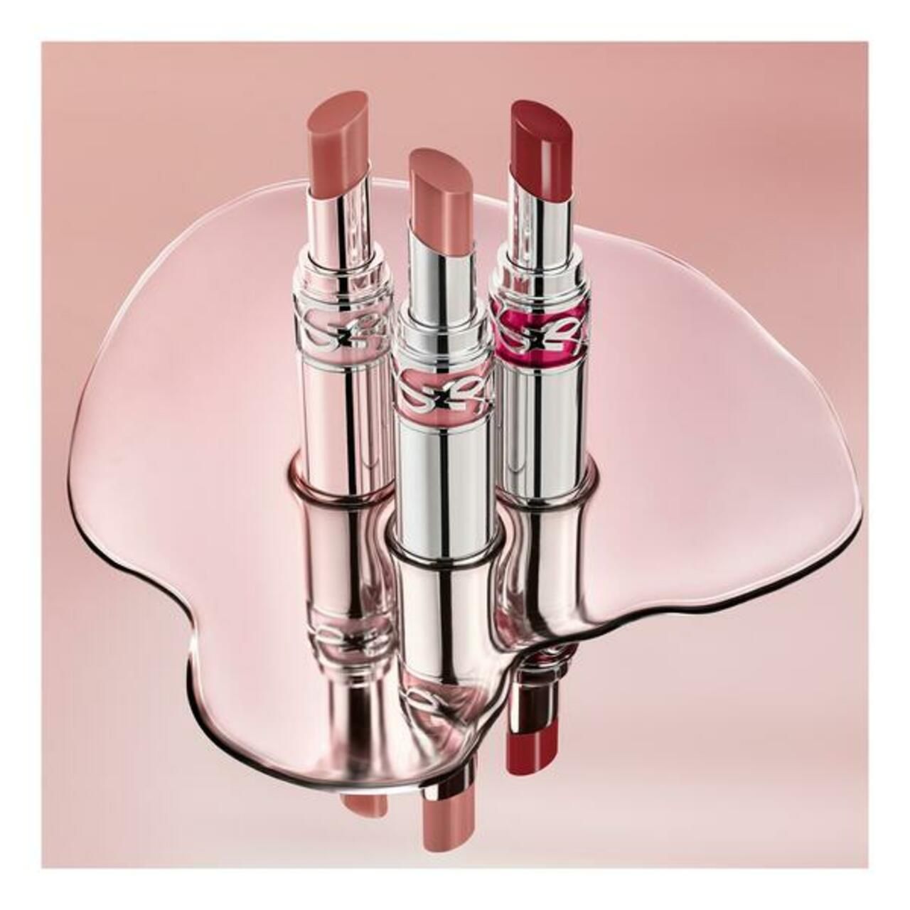 Drei Yves Saint Laurent Loveshine Candy Glaze Lippenstifte auf einer spiegelnden Oberfläche.