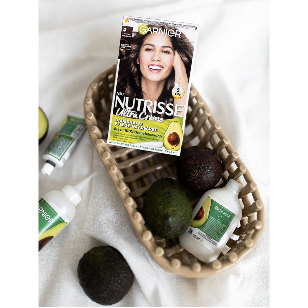 Produkt-Arrangement mit Garnier Nutrisse Ultra Creme. Avocado, Behälter, und Zubehör in einem Korb. Auf hellem Untergrund.