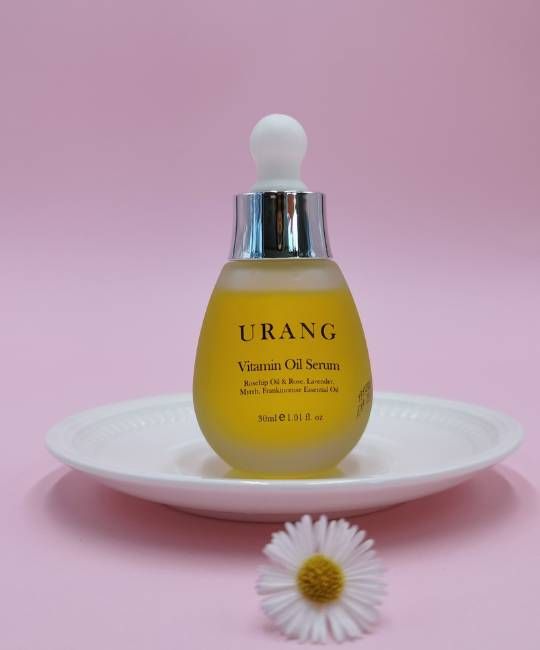 Flacone di vetro giallo con tappo bianco e collo argentato, su piatto bianco. Scritta: URANG Vitamin Oil Serum.