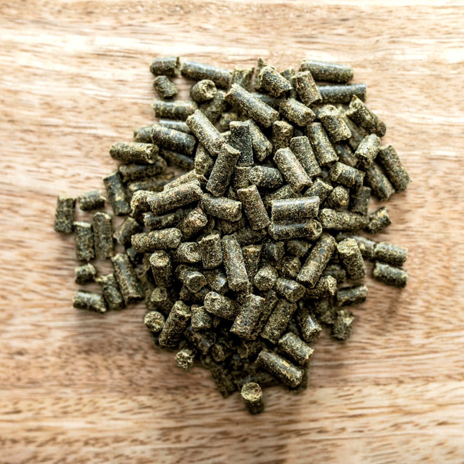 Haufen von zylindrischen, grünen Pellets auf Holzuntergrund. Nahaufnahme, Draufsicht.