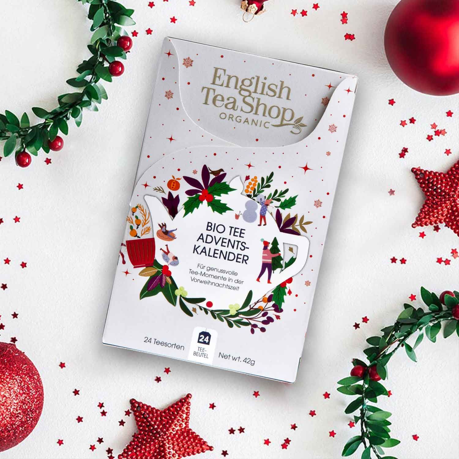 Adventskalender mit Logo und Aufschrift. Weihnachtsdekoration im Hintergrund. Rote Sterne und Kugeln.