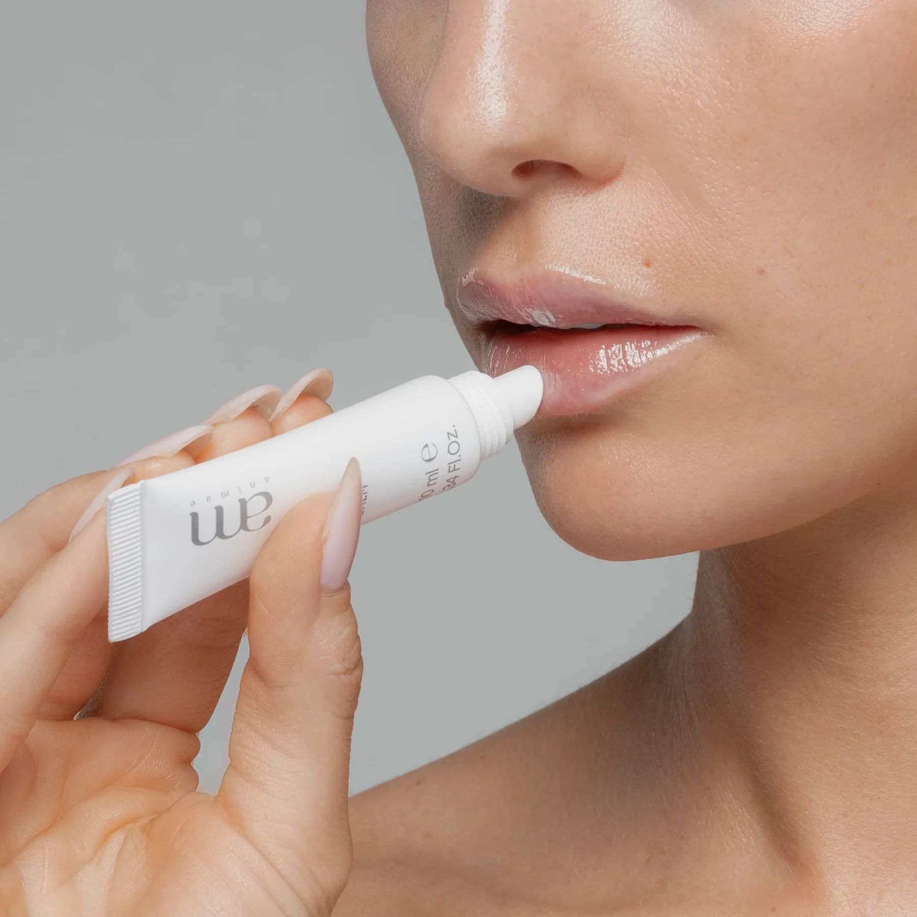 Una persona applica un prodotto da un tubetto bianco con il logo "am" sulle labbra. Il tubetto indica "10 ml e".