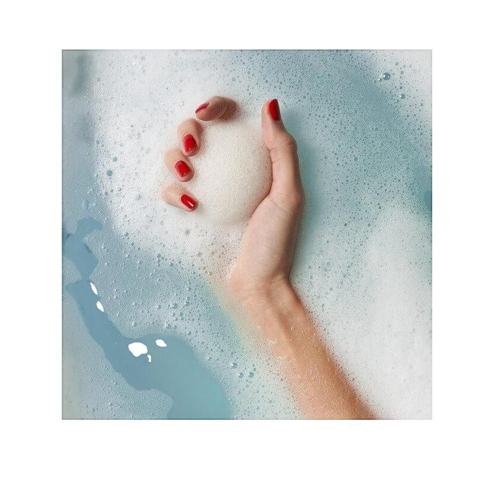 Hand hält Konjac-Schwamm in Seifenwasser. Rote Fingernägel. Wasser blau und schaumig.