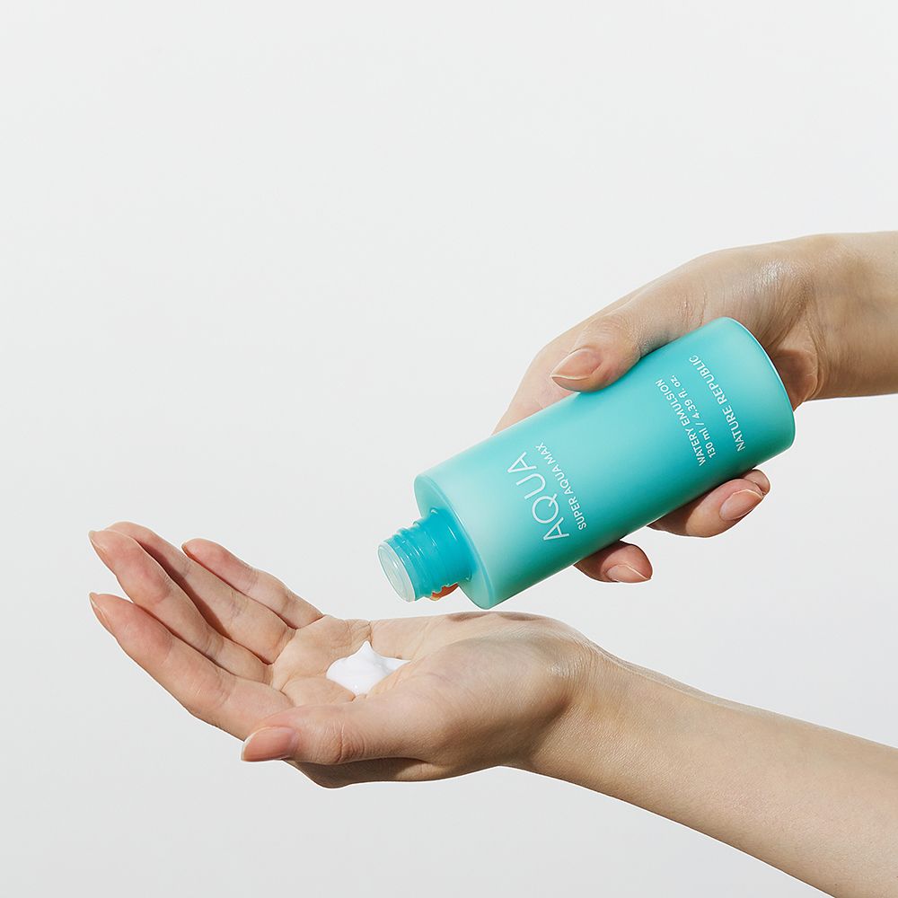 Hände halten eine türkisfarbene Flasche und geben eine weiße Emulsion ab. Produkt: AQUA Super Aqua Max Watery Emulsion.