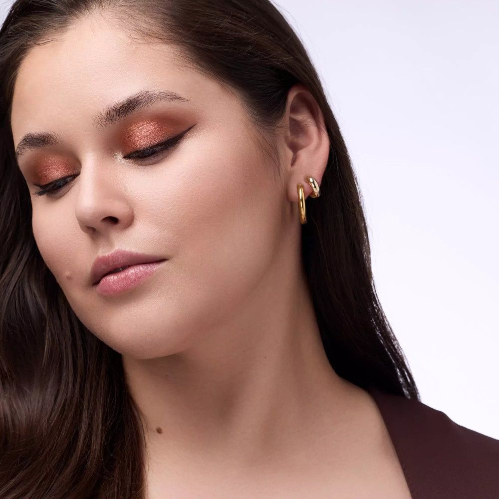 Porträt einer Frau mit Lidschatten. Farben: Orange und Braun. Sie trägt goldene Ohrringe. Dunkle Haare.