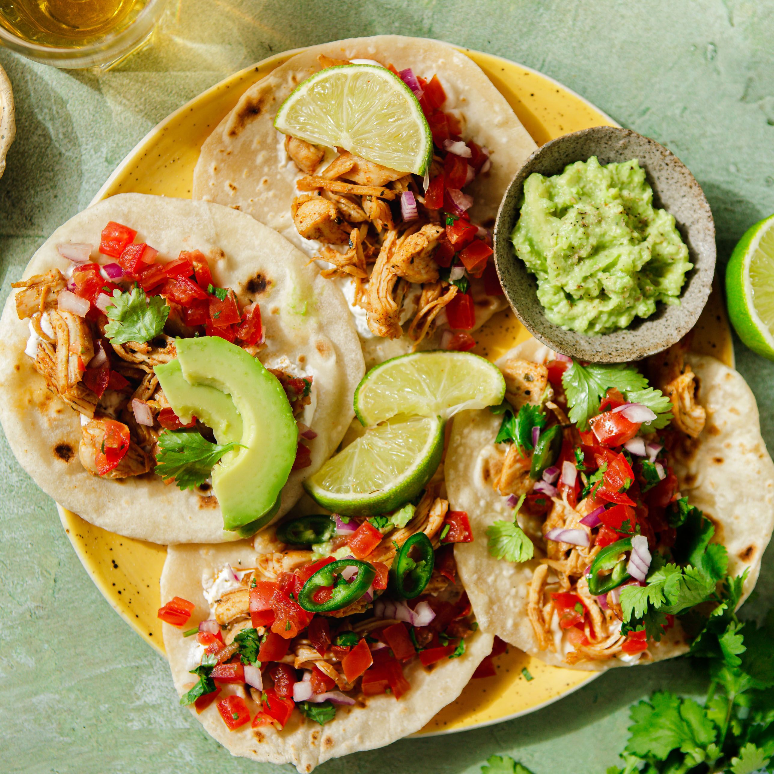 Tacos mit Hühnchen, Tomaten, Avocado und Limette. Guacamole-Schüssel. Koriander.