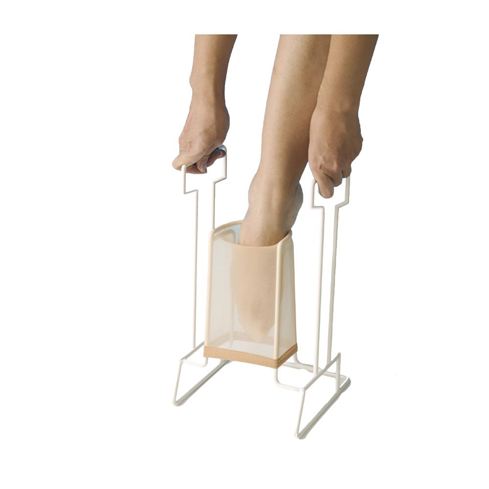 Fuß in einem Strumpfanzieher. Beige Strumpf in einem weißen Metallrahmen. Hände halten den Rahmen. Füße werden in den Strumpf geführt.