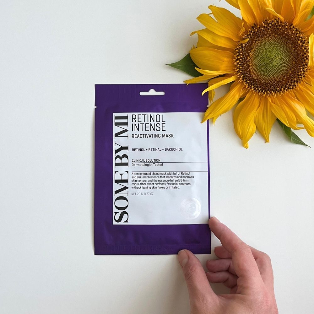 Verpackung einer Gesichtsmaske mit Retinol und Bakuchiol, gehalten von einer Hand neben einer Sonnenblume.
