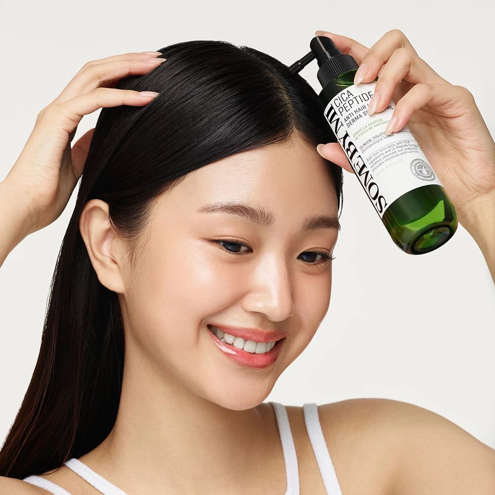 Eine Person hält eine grüne Flasche mit schwarzem Sprühkopf. Aufschrift: Cica Peptide Anti Hair Loss Derma Scalp Tonic.