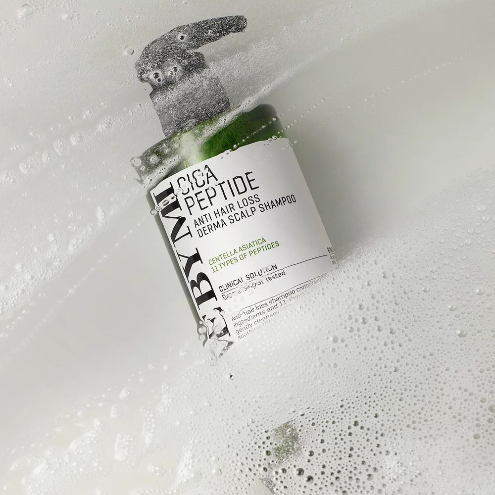 Grüne Shampoo-Flasche mit Pumpe in Seifenblasen. Aufschrift: Cica Peptide Anti Hair Loss Derma Scalp Shampoo.