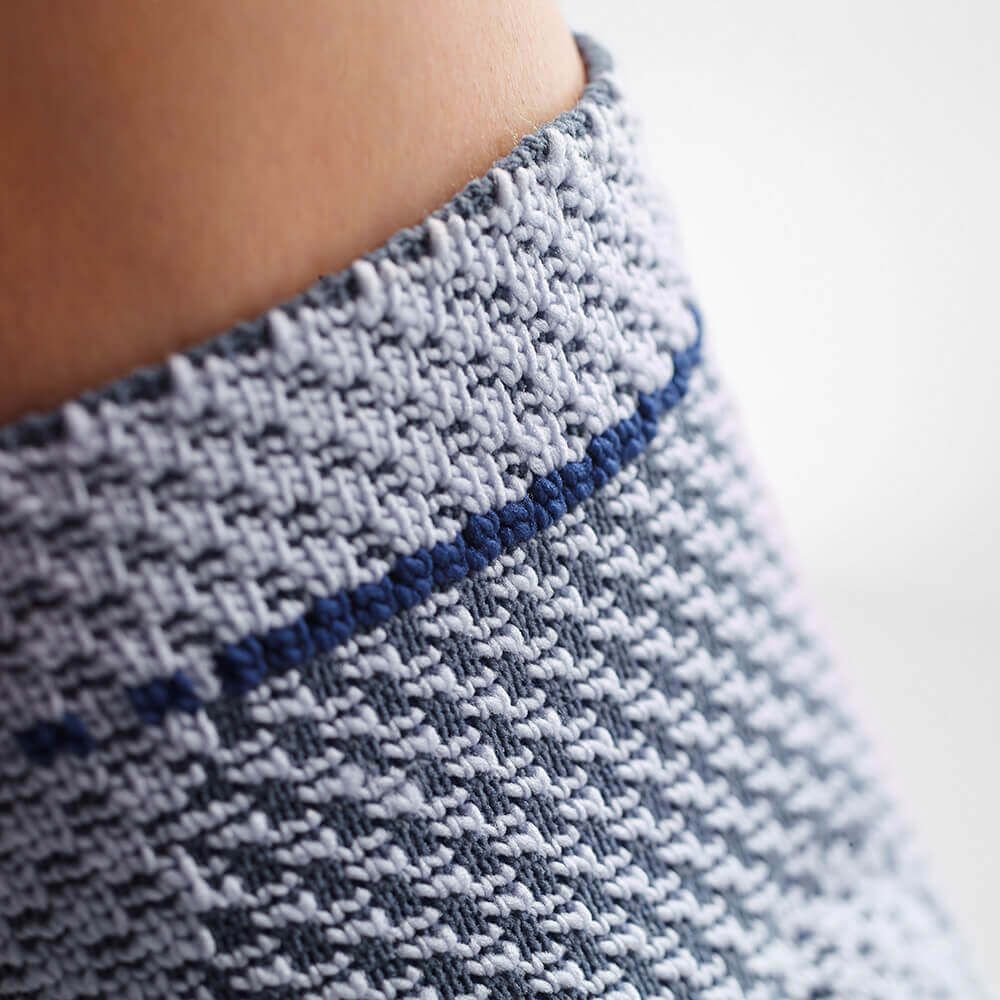 Nahaufnahme der Knöchelbandage, grau-blaues Strickmuster. Ohne Text.