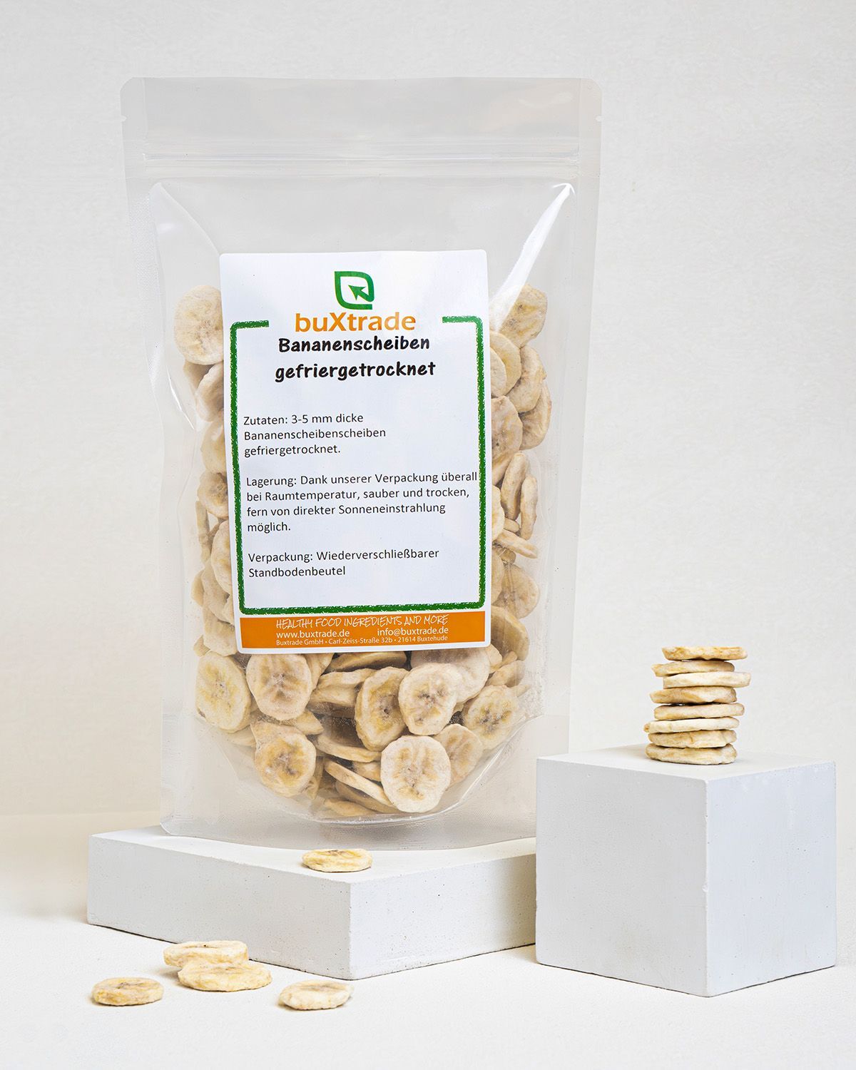 Transparente Verpackung mit gefriergetrockneten Bananenscheiben. Etikett mit Produktinformationen. Stapel Bananenscheiben daneben.
