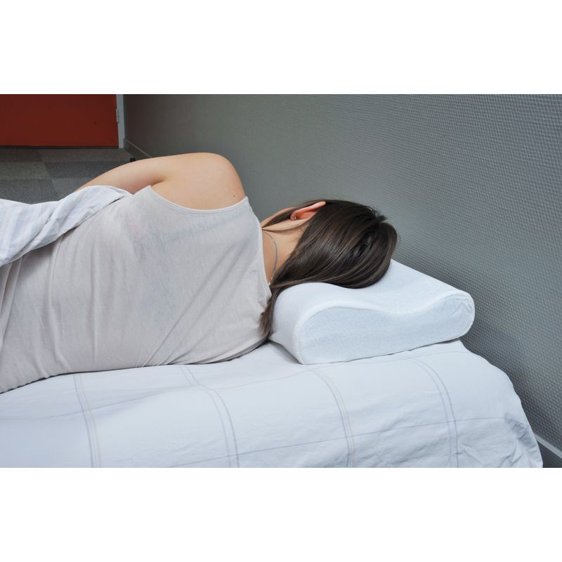 Una persona è sdraiata su un letto bianco, che utilizza un cuscino cervicale ergonomico bianco. Il cuscino ha una forma ondulata e sostiene il collo.