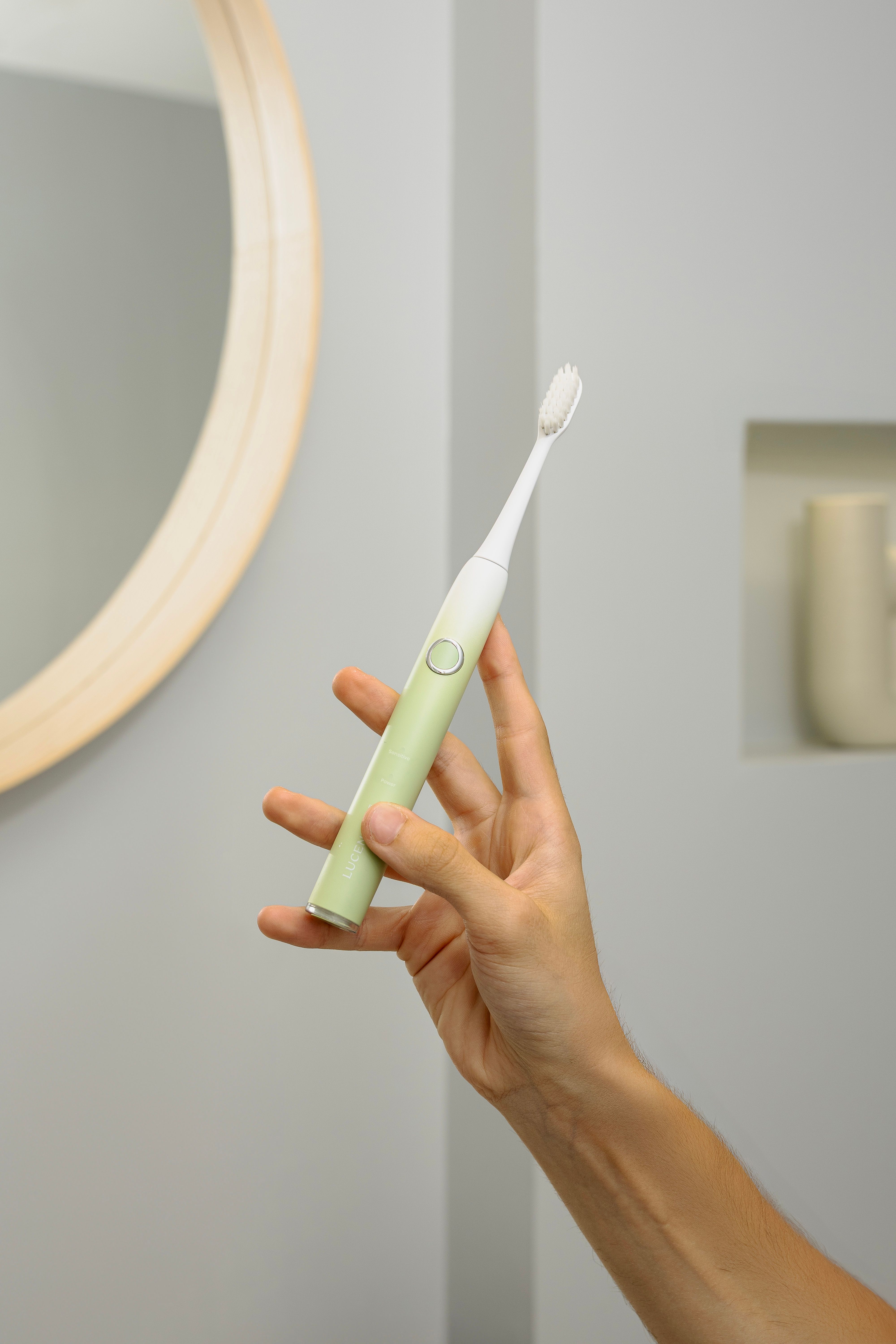 Hand hält grüne elektrische Zahnbürste. Spiegel und Badezimmerhintergrund.