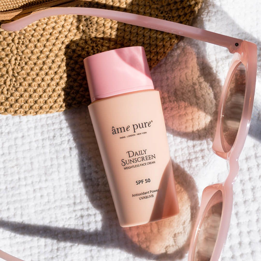 Âme Pure Daily Sunscreen Flasche neben Sonnenbrille und Tasche, SPF 50.