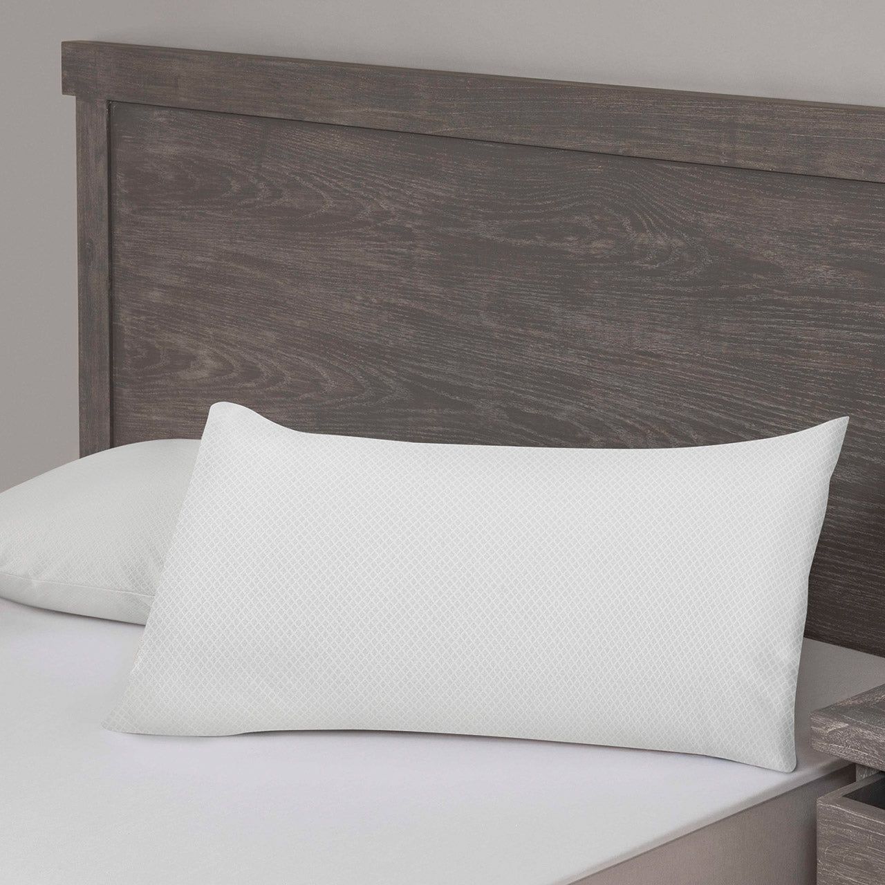 Weißes Kissen mit Rautenmuster auf einem Bett mit Holzkopfteil.